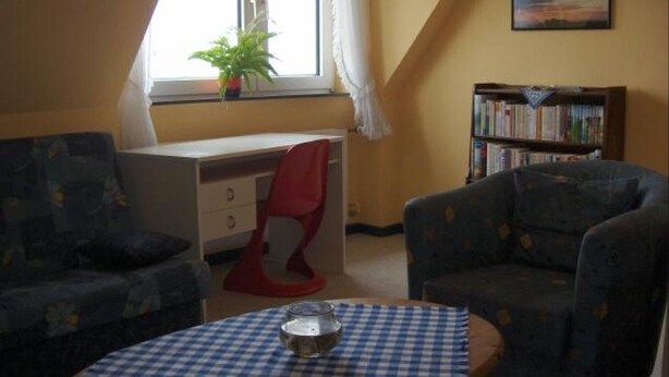Une pièce comprenant un bureau, deux fauteuils, une bibliothèque et une fenêtre avec une plante.