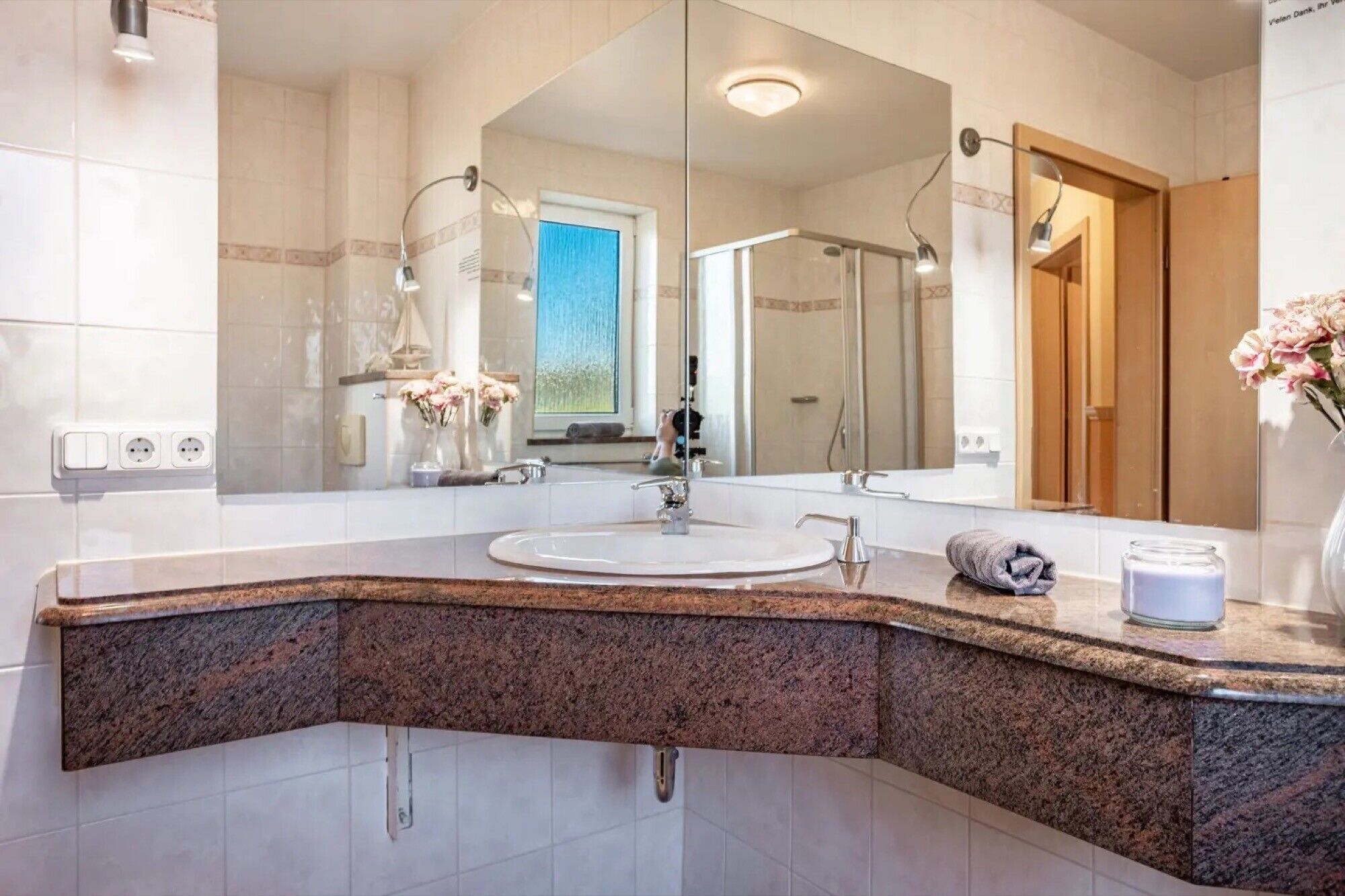 Een moderne badkamer met een grote spiegel, een granieten aanrechtblad en een douche.