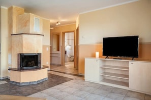 A living room with a fireplace, a television on a stand, and a hallway leading to a bathroom. - Apartment 'Habichtssicht' with Lake View, Shared Terrace and Wi-Fi (Buschvitz)