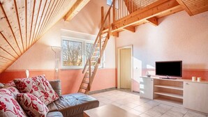 Quarto estilo loft com escada de madeira, um sofá, uma TV e uma pequena mesa.