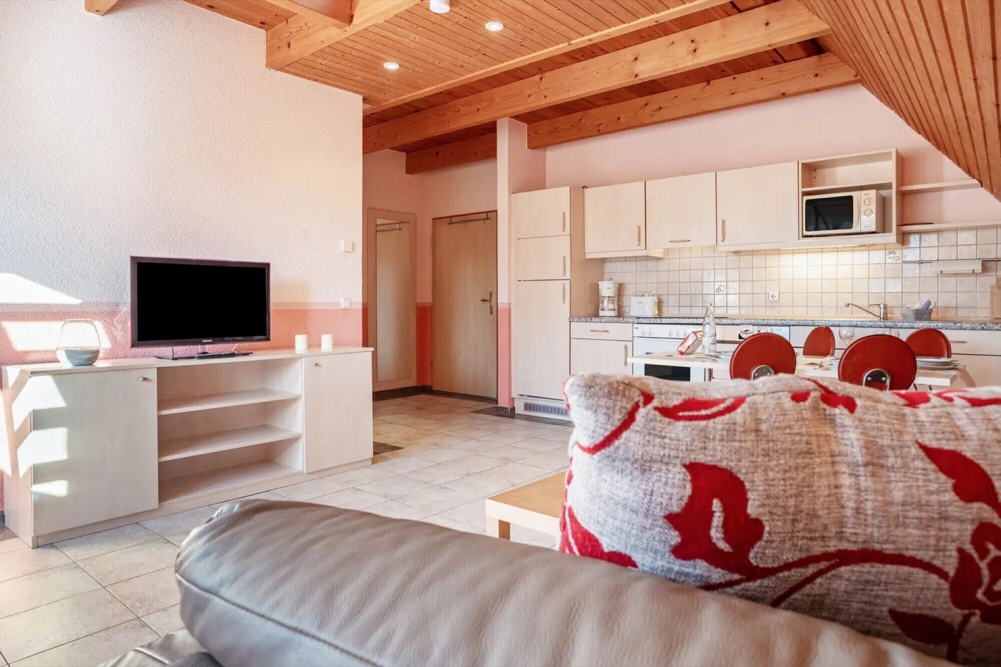A modern living room with a flat-screen TV, a sofa, and a kitchen in the background.
