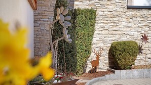 Un mur de pierre orné d’une sculpture de cerf, une haie taillée avec soin et un jardinière remplie de fleurs.