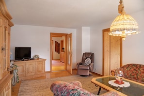 A living room with a television, a sofa, a recliner, a glass coffee table, and a wooden cabinet.