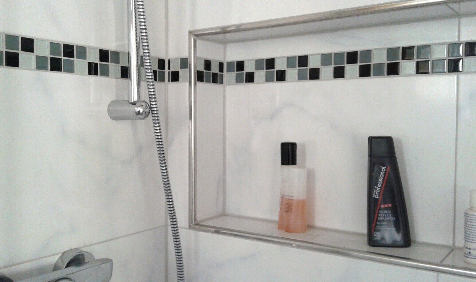 A bathroom with a shower, a mirror, and a shelf with toiletries.
