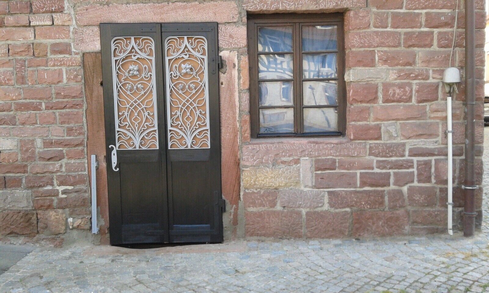 Ein Backsteinhaus mit doppeltürigem Eingang, verziert mit aufwendender Metallverzierung, und einem kleinen Fenster mit Gittermuster.