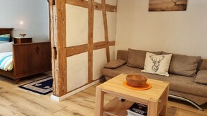 Ein Zimmer mit Holzboden, einem Bett mit blau-weiß gestreifter Bettdecke, einem hölzernen Schminktisch, einem braunen Sofa mit einem Deer-Kissen und einem kleinen Holztisch mit einer Schüssel.