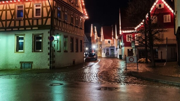 Eine beleuchtete Straße mit Kopfsteinpflaster und Häusern bei Nacht.