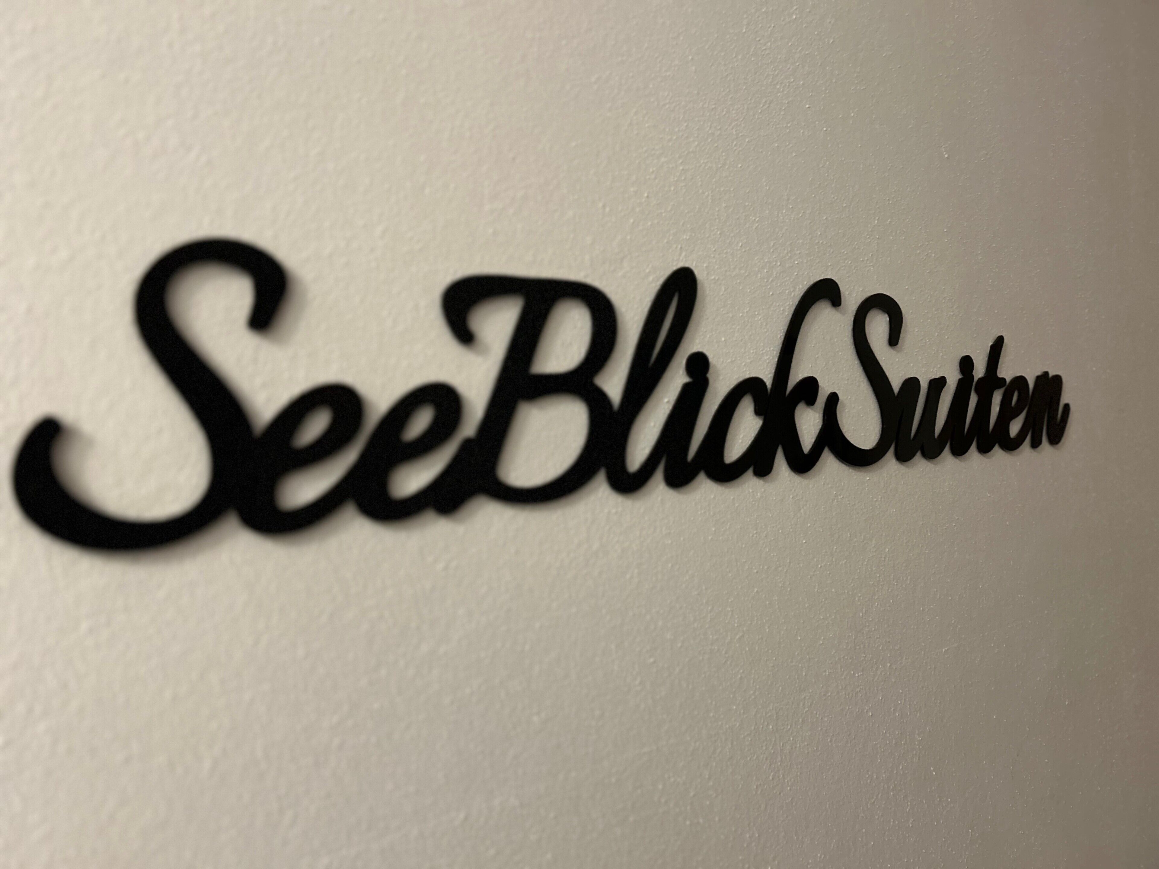 Ein Schild mit dem Schriftzug 'SeeBlckSuiten' an einer weißen Wand.