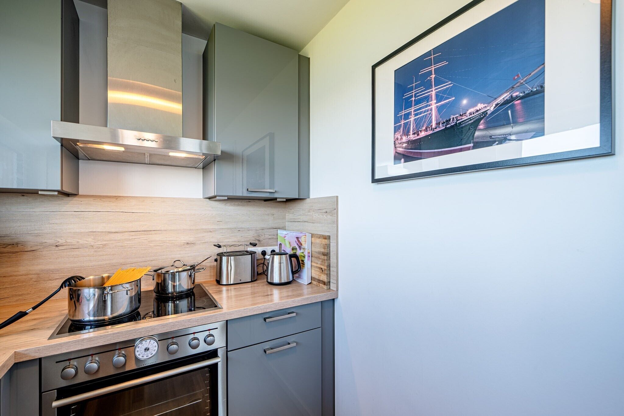 A modern kitchen with stainless steel appliances, wooden countertops, and a framed maritime painting.