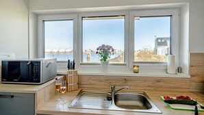 A modern kitchen with a built-in microwave, a stainless steel sink, and a window with a view of a body of water and buildings. - Holiday Home 'Am Meer' with Sea View, Private Terrace and Wi-Fi (Kappeln)