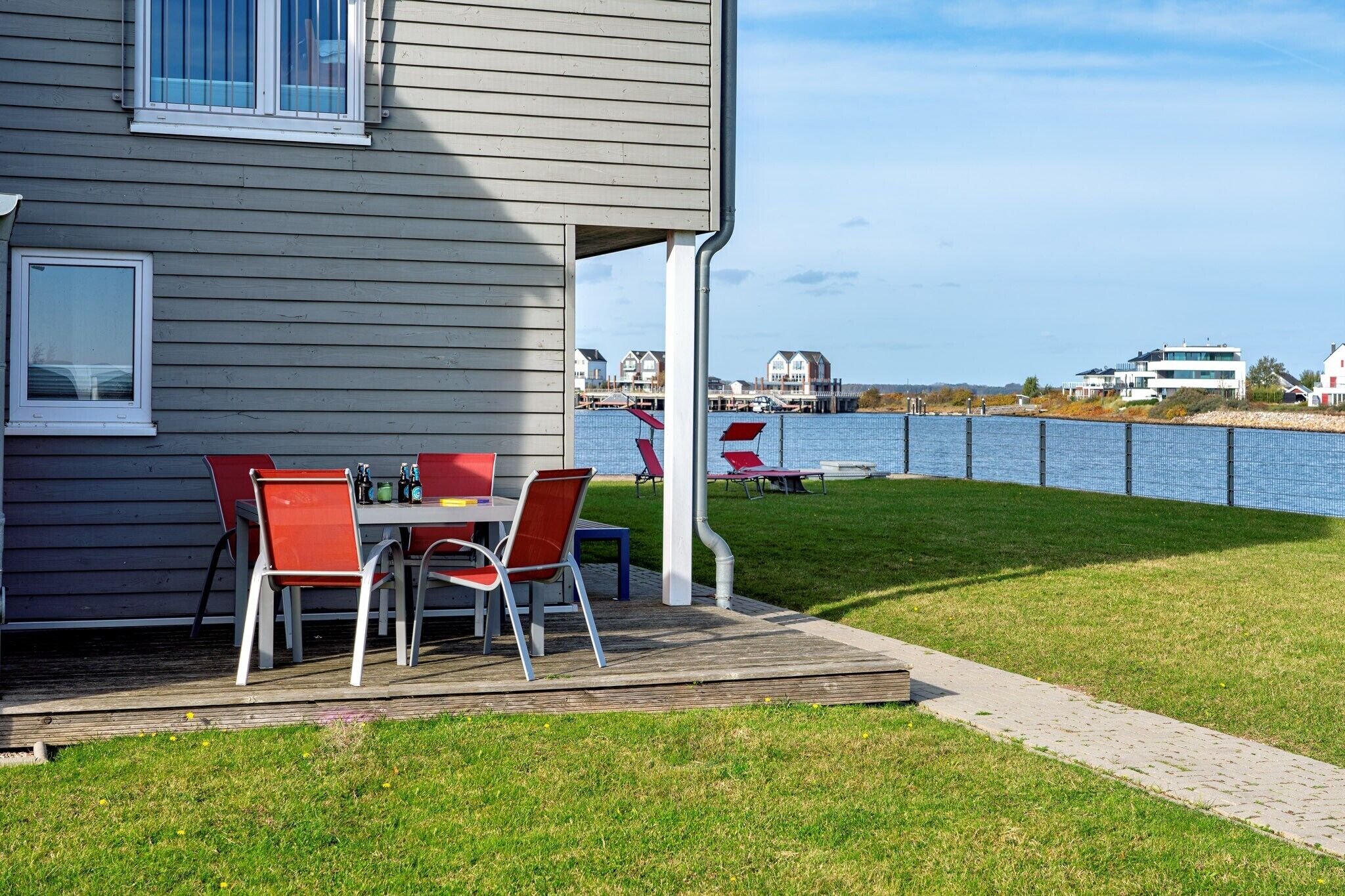 A house with a deck, a table with chairs, and a view of a body of water and buildings in the background.