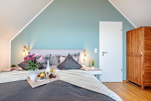A bedroom with a sloped ceiling, a bed with a quilted bedspread, a bedside table with a lamp, a wooden wardrobe, and a small plant on the nightstand. - Holiday Home 'Am Meer' with Sea View, Private Terrace and Wi-Fi (Kappeln)