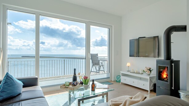 Un salon comprenant un canapé, une table basse en verre, une cheminée, un téléviseur et un balcon avec vue sur la mer.