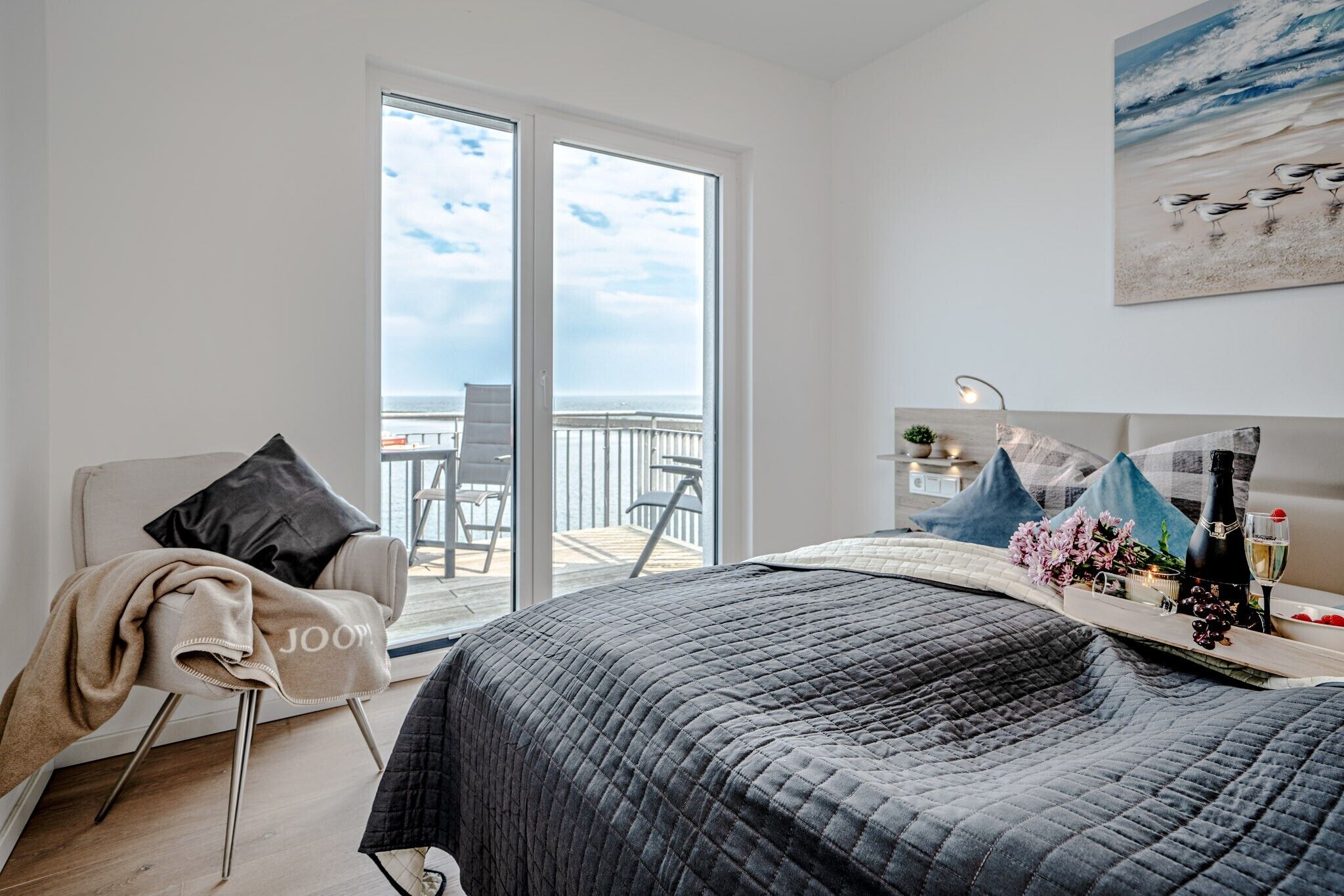 Ein Schlafzimmer mit Bett, einem Sessel, einem Balkon und einem Gemälde.