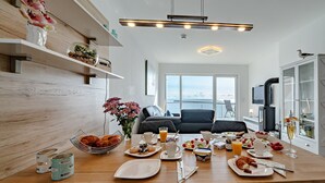 Un coin repas avec une table en bois mise pour le petit-déjeuner, un canapé et une vue sur la mer.