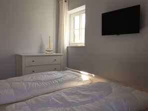 Ein Schlafzimmer mit Bett, Schminktisch, Fenster und Flachbildfernseher.