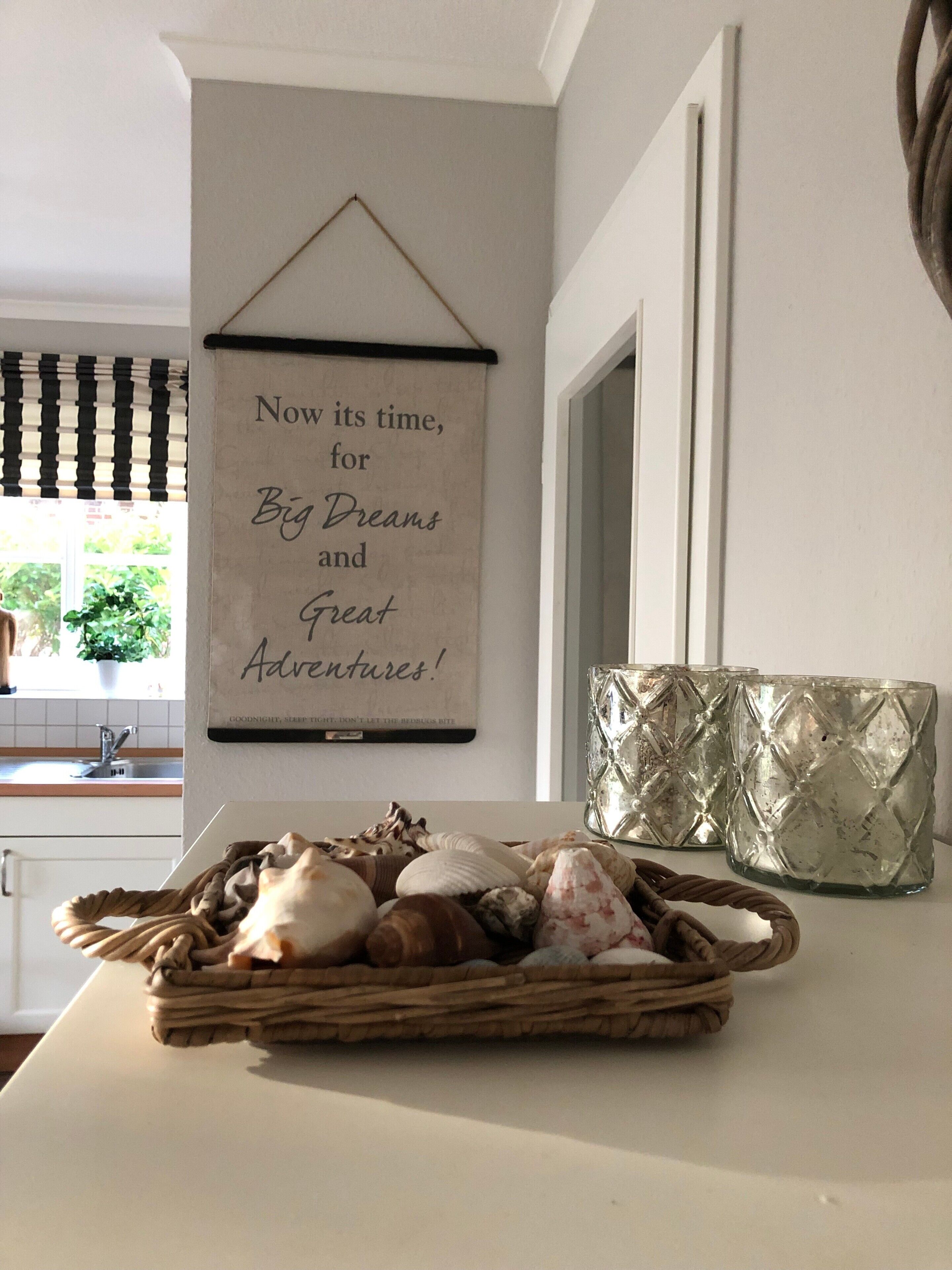 A kitchen with a wall-mounted sign, a basket of seashells, and decorative glassware.