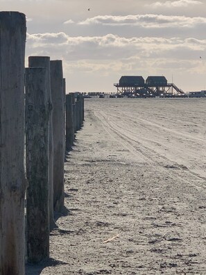 A sandy beach with wooden posts, a pier structure, and vehicles in the background. - Apartment 'Urlaubsdomizil Dünenhof' with Private Terrace, Shared Garden and Wi-Fi (Sankt Peter-Ording)