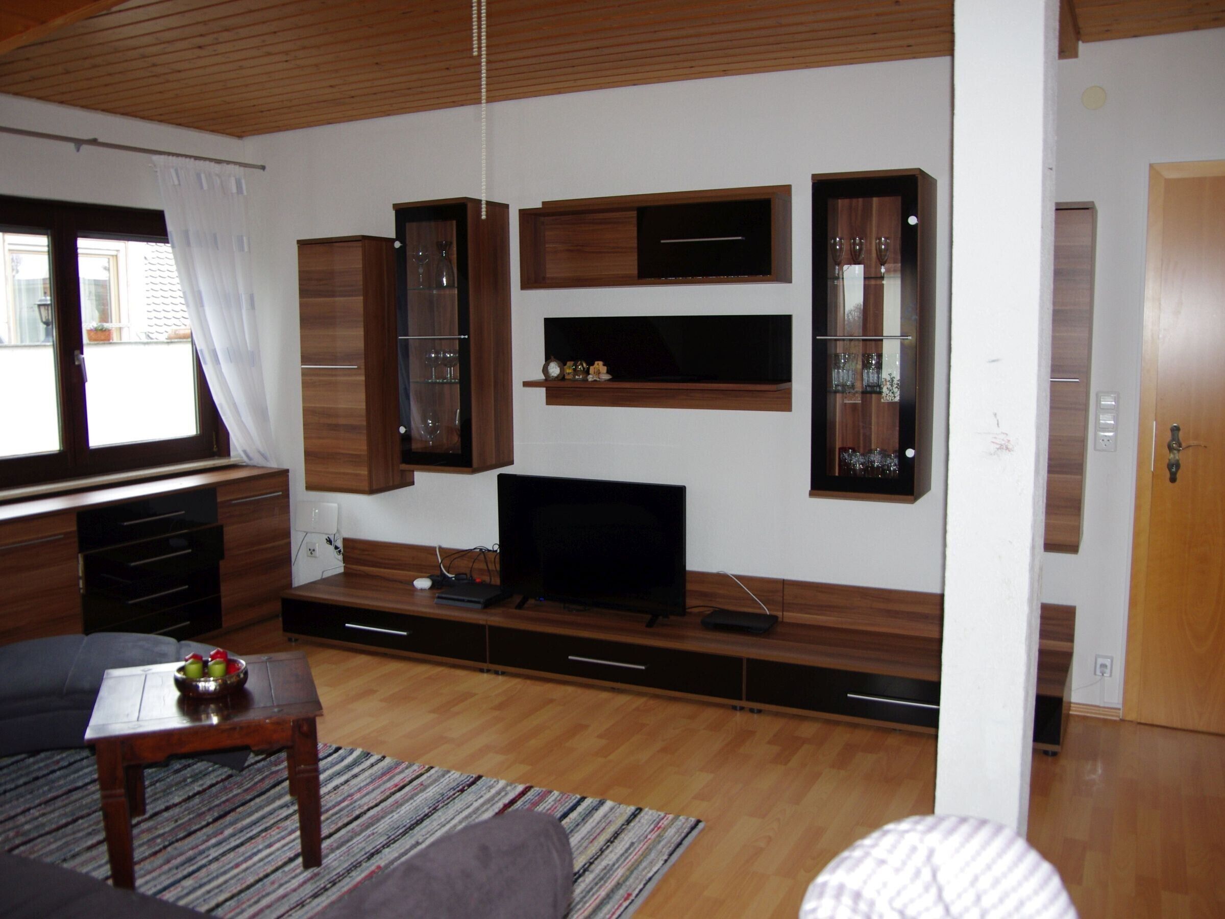 Een woonkamer met een televisie, houten kasten, een bank en een raam met gordijnen.