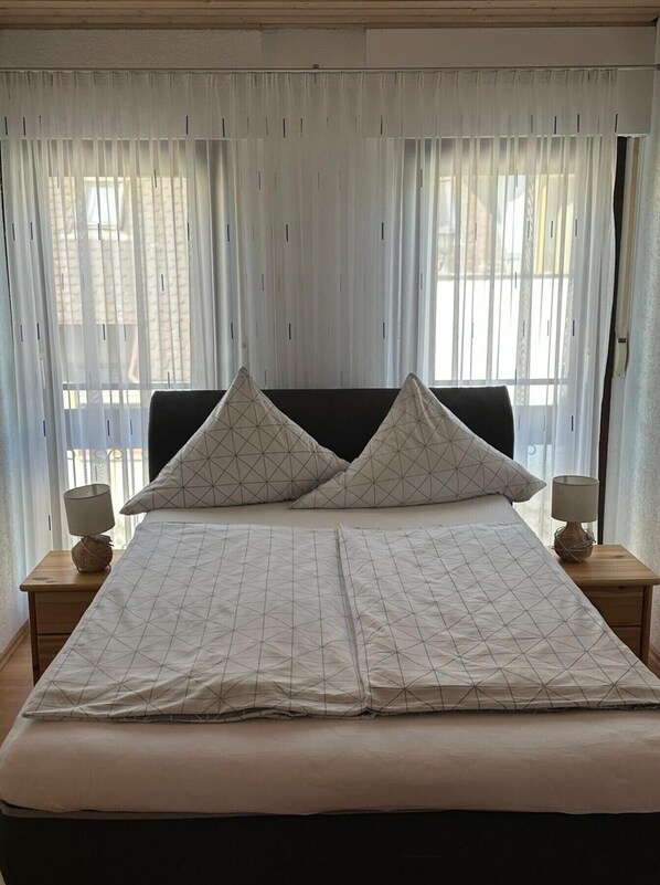 Un lit avec une couvre-lit à motifs géométriques, deux oreillers assortis et une tête de lit en bois.
