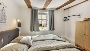 Een slaapkamer met een bed, een radiator, een raam met gordijnen, een houten kledingkast en een wandlamp.
