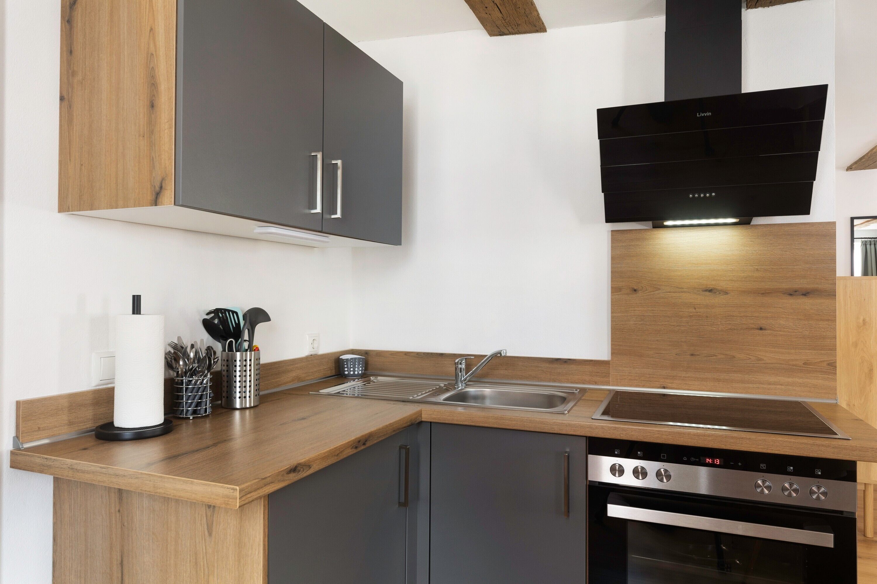 Una cocina moderna con horno empotrado, pileta de acero inoxidable y alacenas de madera.