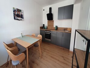 Una cocina compacta con una mesa y sillas, una cafetera, estufa y pileta.
