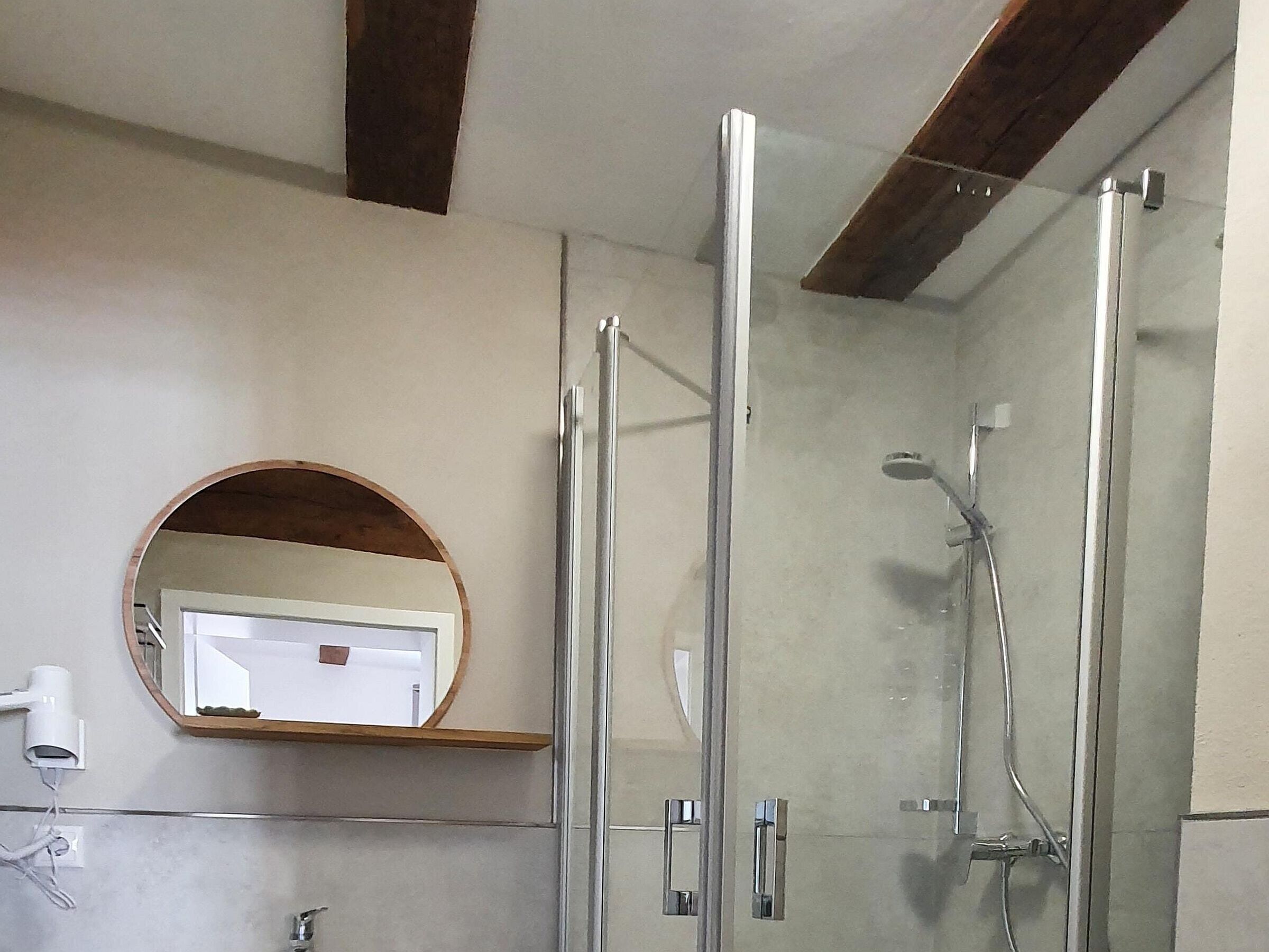 A bathroom with a glass shower enclosure, a round mirror, and a white towel rack.