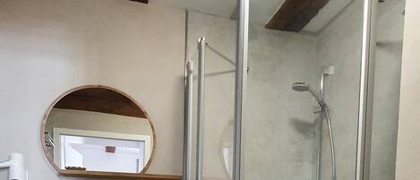 A bathroom with a glass shower enclosure, a round mirror, and a white towel rack.