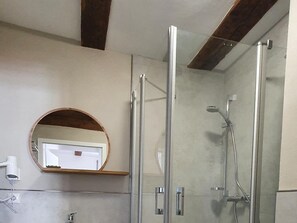 Une salle de bain avec une douche à parois de verre, un miroir rond et un porte-serviettes blanc.