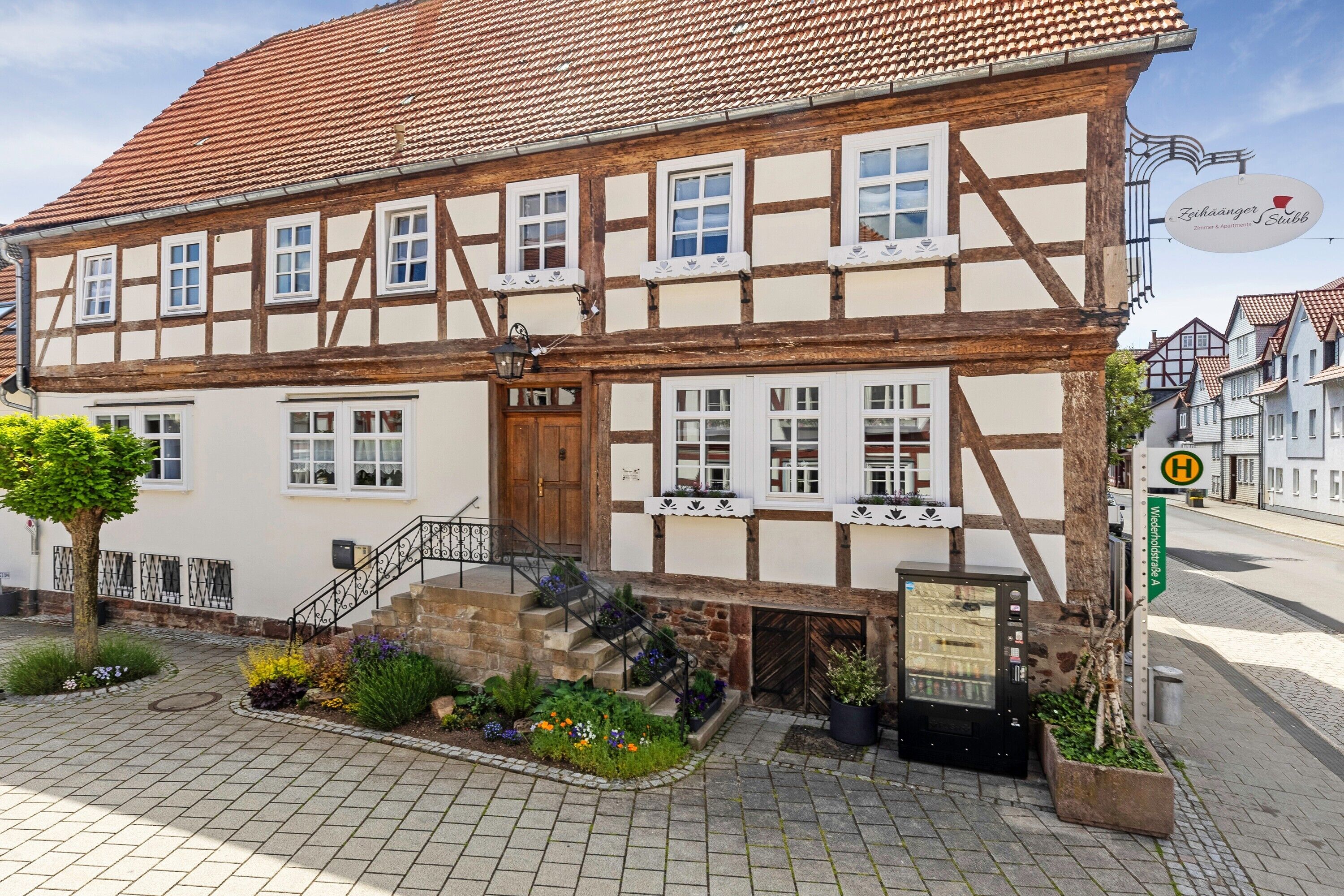 Ein traditionelles Fachwerkhäuschen mit Treppe, einem Schild und einem kleinen Garten.