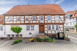 Il s’agit d’un bâtiment traditionnel à colombages, doté d’un toit en tuiles, d’une porte en bois et d’un petit jardin agrémenté de plantes en pot.