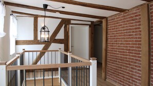A wooden staircase with black railings, a hanging light fixture, and a brick wall. - Zeihäänger Stubb Double Room '8' with Wi-Fi (Schwalmstadt)