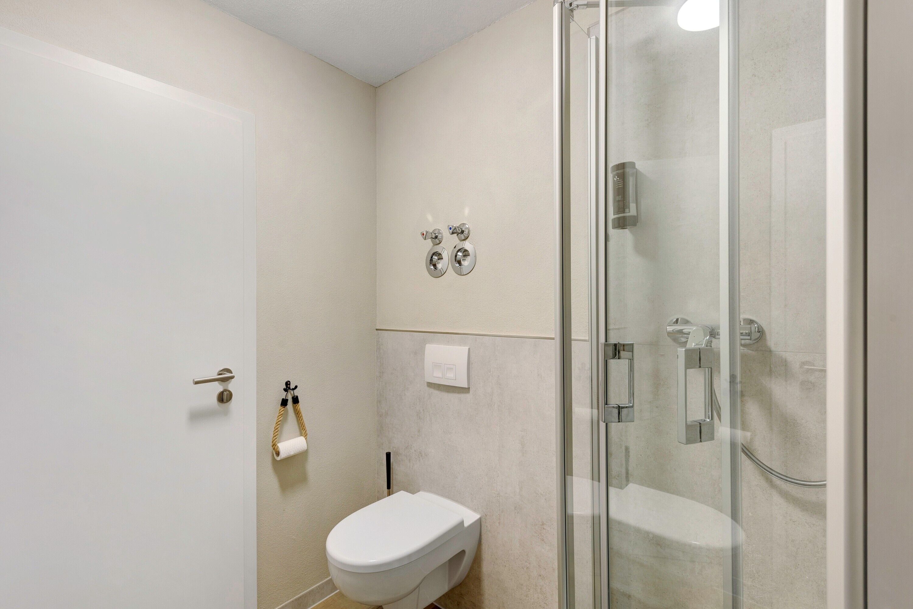 Ein Badezimmer mit Toilette, Dusche und einer Duschkabine aus Glas.