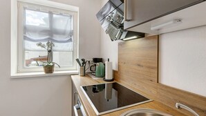 Una cocina moderna con estufa integrada, un lavamanos y una ventana con cortinas de gasa.