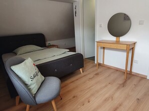 Ein Schlafzimmer mit einem Bett, einem Sessel, einem kleinen Tisch und einem Wandspiegel.