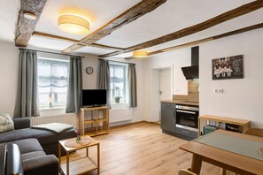 Uma sala de estar moderna com sofá, TV, mesa de centro de madeira e uma área de cozinha com fogão e forno.