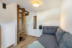 Ett rum med en säng, ett element, synliga träbjälkar, en spegel och en väggmonterad lampa.