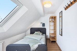 Une chambre avec un puits de lumière, un lit avec des oreillers, une table de chevet, un luminaire suspendu et une étagère en bois.