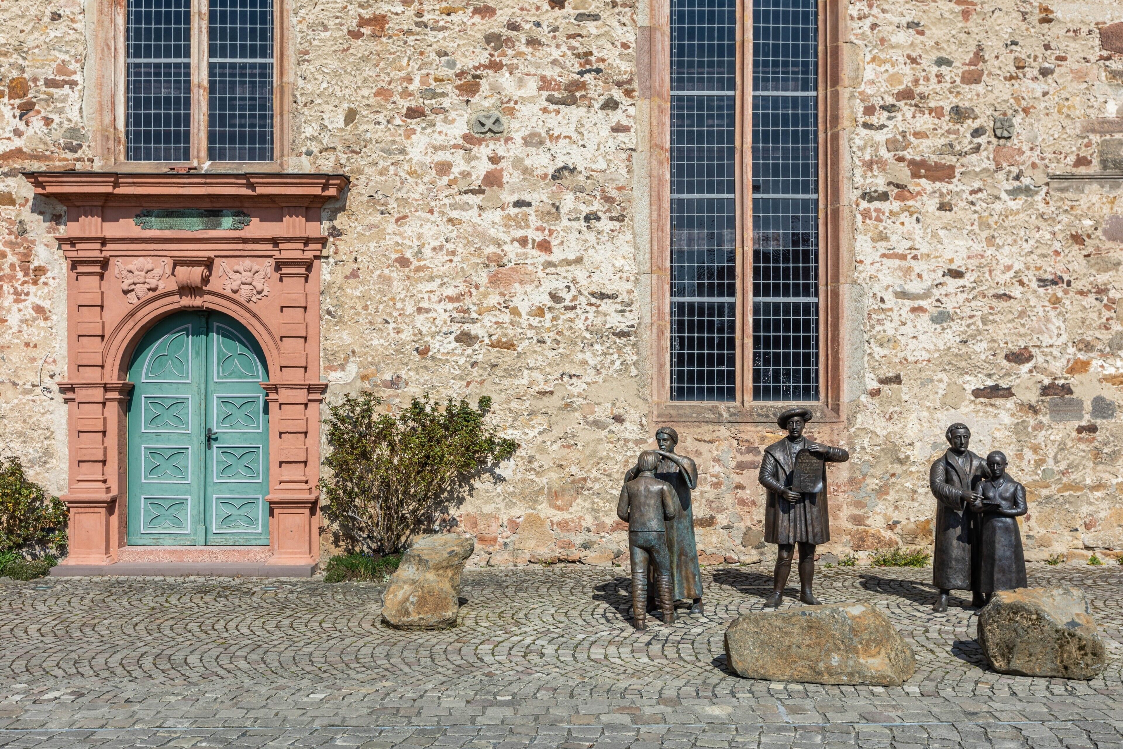 Un edificio de fachada de piedra, con una puerta verde y una estatua de un hombre y una mujer.