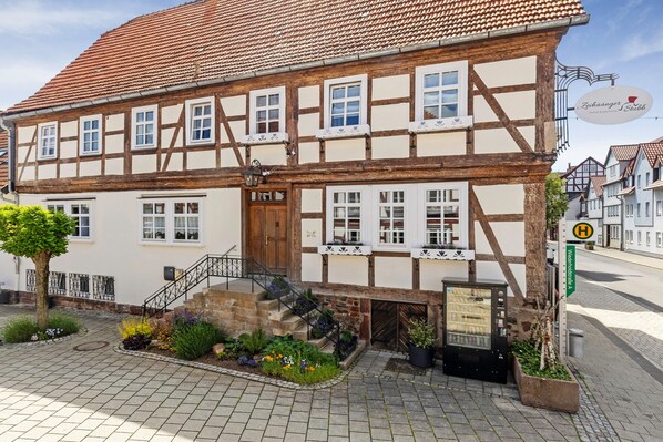 A traditional half-timbered building with a staircase, a signboard, and a small garden area.