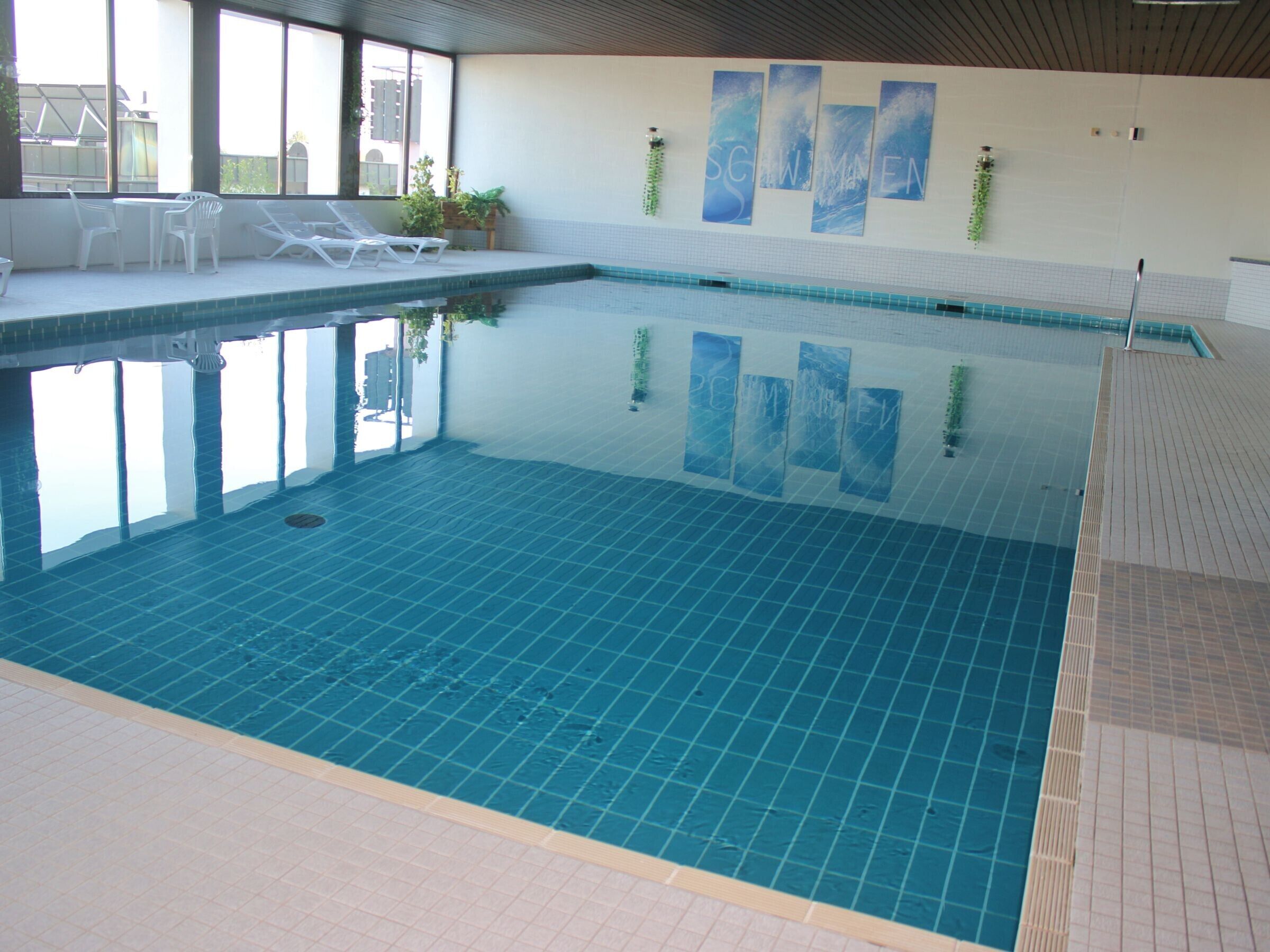 Een binnenzwembad met helder water, betegelde vloer en ligbedden.