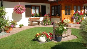 A wooden building with a bench, hanging flower baskets, and potted plants. - Apartment 'Gartenblick' with Mountain View, Private Terrace and Wi-Fi (Sankt Peter)