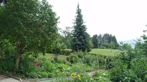 A garden with various plants and flowers, a paved walkway, and a large tree. - Apartment 'Gartenblick' with Mountain View, Private Terrace and Wi-Fi (Sankt Peter)
