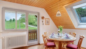 A dining area with a round table, wooden chairs, a view of a green landscape, a wooden ceiling, and a window. - Apartment 'Blumenwiese, 80qm' with Mountain View, Shared Terrace and Wi-Fi (Sankt Peter)