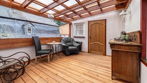 A covered patio with wooden flooring, a chair, a small table, and a cabinet. - Holiday Home 'Moseljuwel' with Sauna, Pool & Large Moselle Terrace (Traben-Trarbach)