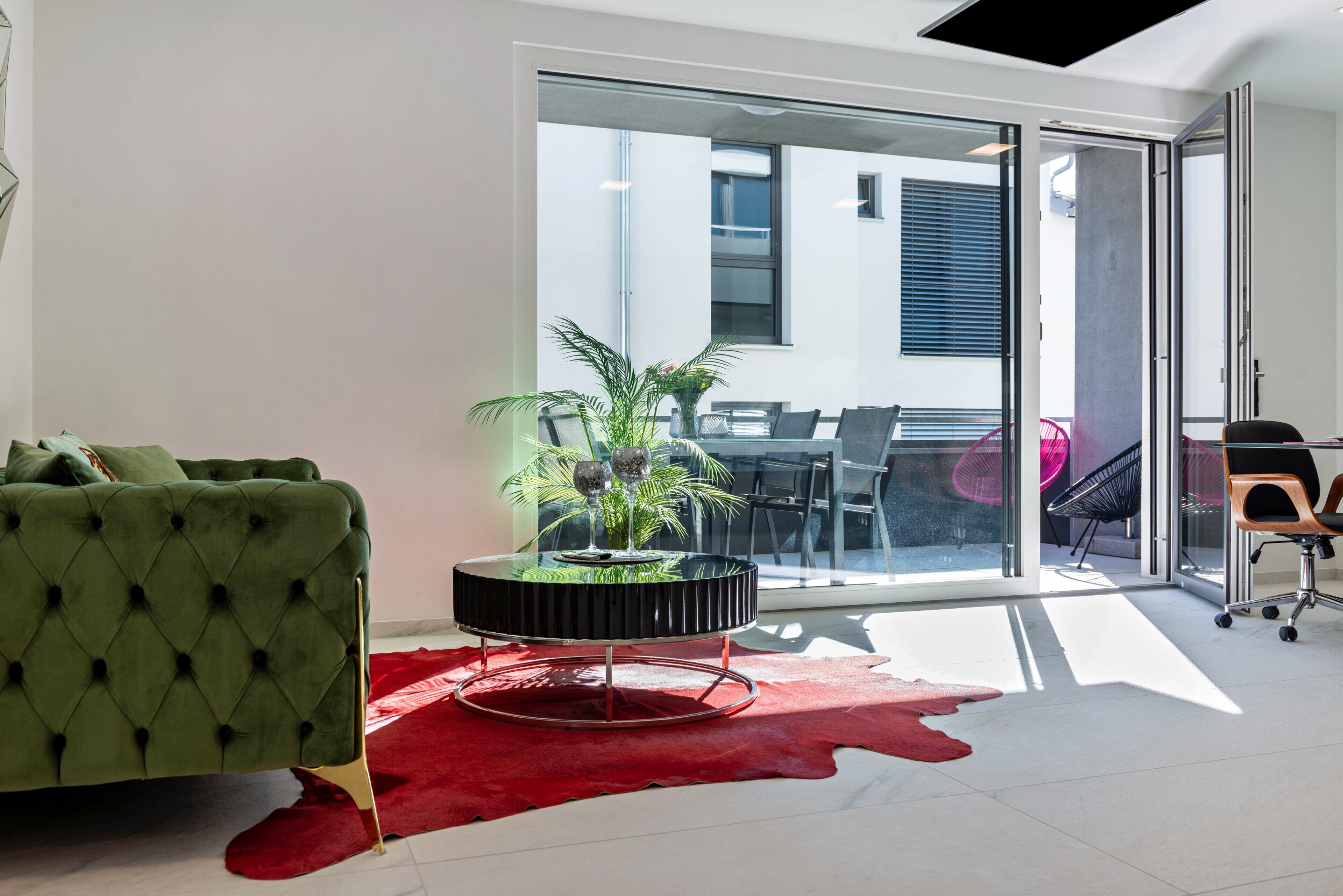 A modern living room with a green tufted sofa, a glass-top coffee table with a plant, and a red rug.