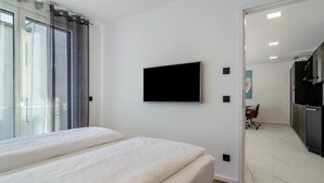 Une chambre à coucher avec un lit, un téléviseur fixé au mur et une vue sur la cuisine et l’espace repas.