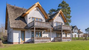 A two-story house with a balcony, a thatched roof, and a well-maintained lawn. - Modern vacation apartment with garden, sauna & whirlpool - ideal for families (Loddin)