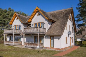 A two-story building with a thatched roof, wooden balconies, and a paved pathway leading to the entrance.